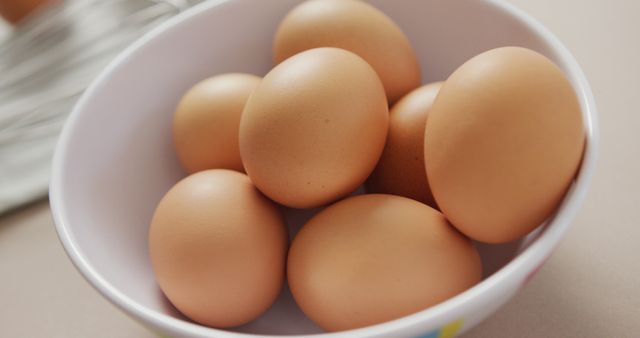 Shows fresh brown eggs in a white bowl resting on a kitchen counter, ideal for use in food blogs, cooking tutorials, healthy eating articles, and advertisements promoting organic and farm-fresh food. The image portrays simplicity and cleanliness, making it perfect for content related to health and wellness.
