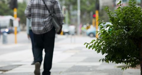 Back-view of african american man walking on city sidewalk carrying shoulder bag near crosswalk