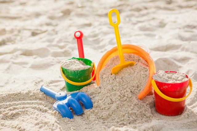Colorful sand buckets and a spade are scattered on a tropical beach, filled with sand. Ideal for illustrating summer vacations, family holidays, and outdoor activities. Perfect for travel brochures, family-oriented advertisements, and articles about beach destinations.
