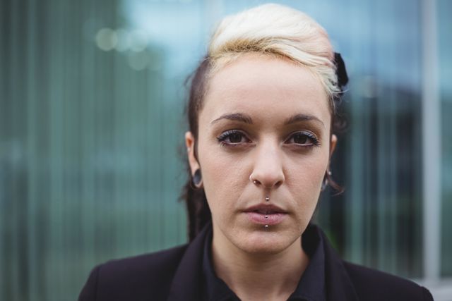 Confident businesswoman with facial piercings standing in office campus. Ideal for use in corporate websites, business presentations, diversity and inclusion campaigns, and modern workplace articles.