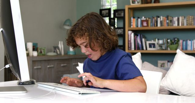 Young boy with curly hair learning to type on keyboard at home. Shows focus and education in technology. Great for use in educational content, technology services, or lifestyle articles focused on children's learning and development.