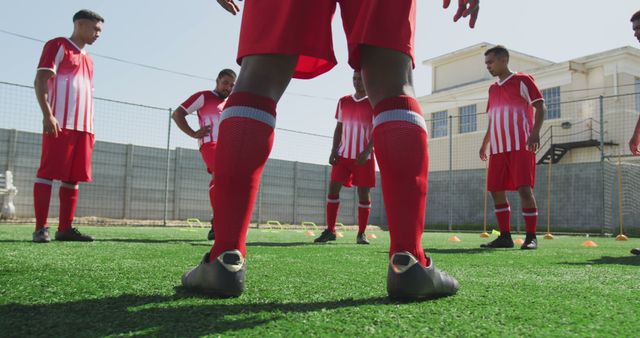 This image depicts a group of soccer players in a team huddle on a training field, wearing red uniforms. It is useful for illustrating teamwork, sports training, athletic strategies, and competitive spirit. Ideal for sports-related articles, team management programs, motivational posters, and training materials.