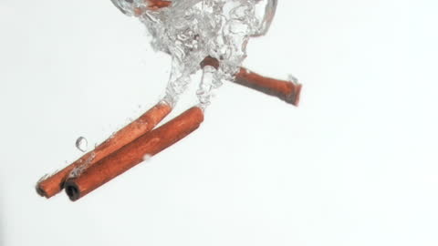 Cinnamon Sticks Splashing into Clear Water in Slow Motion