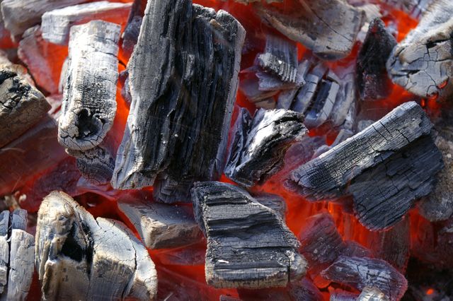 Highly detailed view of embers glowing underneath chunks of charcoal, illustrating heat and texture. Perfect for use in articles or advertising related to camping, barbecues, grilling, outdoor activities, or fire safety. Useful for educational materials on combustion or the science of heat.