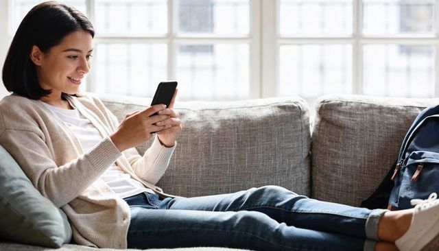 Young woman reclining on sofa using smartphone for messaging, relaxing home lifestyle