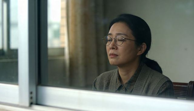 Asian woman gazing through window wearing round glasses, knit vest and button-down