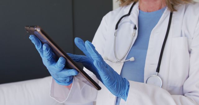 Healthcare professional with stethoscope using digital tablet, enhancing patient care with technology. Gloves indicate a clean, sterile environment. Useful for topics on medical innovation, telehealth, patient data management, and modern healthcare practices.