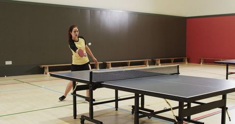 Woman Playing Table Tennis Energetically in Indoor Sports Facility