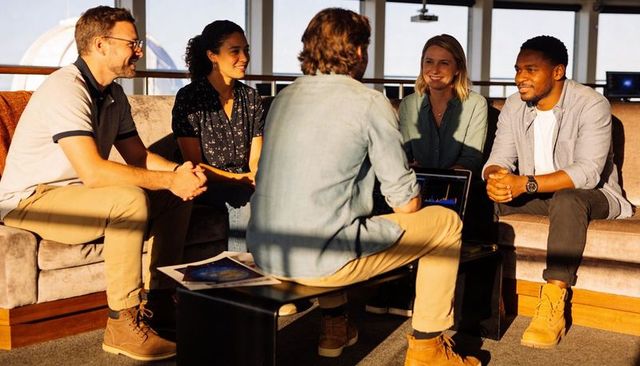 Five colleagues collaborating around laptop on sofa, brainstorming in modern startup office