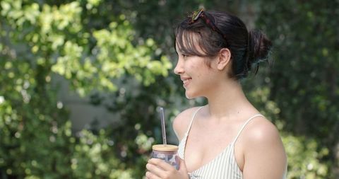 Young Woman Relaxing Outdoors Holding Reusable Cup with Straw