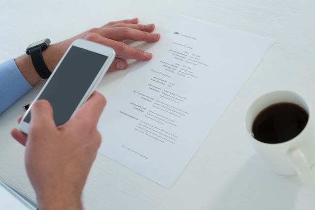 Cropped hands of businessman using mobile phone while holding document at table