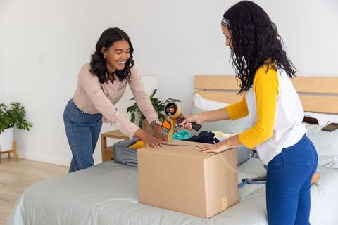 Mother and teenage daughter packing and sealing moving box together in cozy bedroom