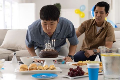 Asian teen celebrating 18th birthday blowing out candles on chocolate cake home party