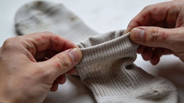 Worn work sock being inspected by hands with scrapes closeup of dirty fabric cuff and grime