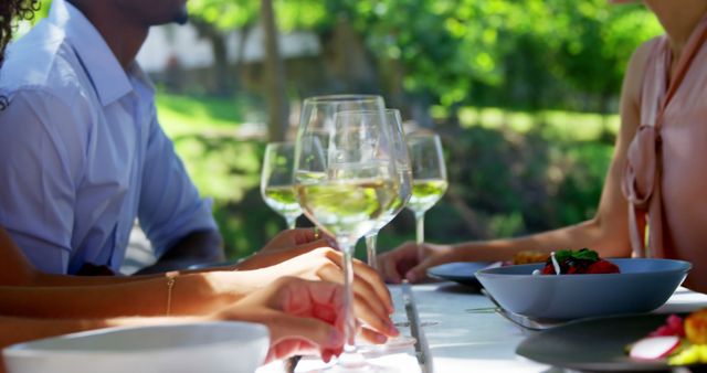 Group of friends having a meal outdoors, enjoying wine and salad in a green and pleasant environment. Ideal for representations of social gatherings, casual dining, summer activities, and leisure time with loved ones. Perfect for websites and advertisements about dining, social events, or outdoor activities best suited for warm seasons.