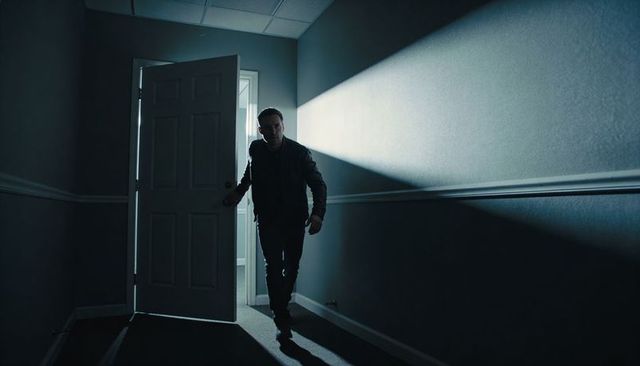 Man stepping through open door into backlit dark corridor, silhouette and shadow drama