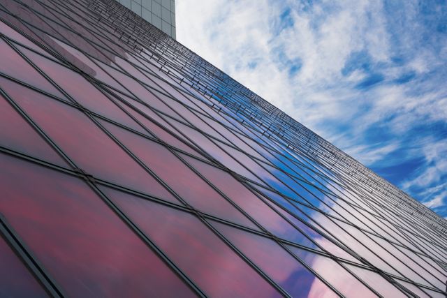 Glass facade reflecting blue sky enhances modern architecture's sleek look. Ideal for use in brochures, architectural portfolios, urban development articles, or as a background for presentations emphasizing modern and contemporary design.