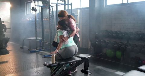 Female trainer embracing client on gym bench providing support and motivation