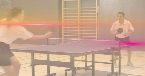 Competitive table tennis rallying in gymnasium with motion blur and colorful lens flare