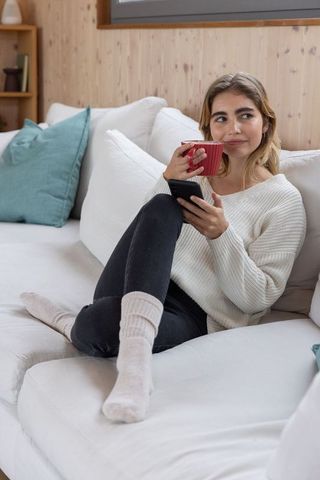 Young Woman Relaxing with Coffee and Smartphone on Modern Sofa