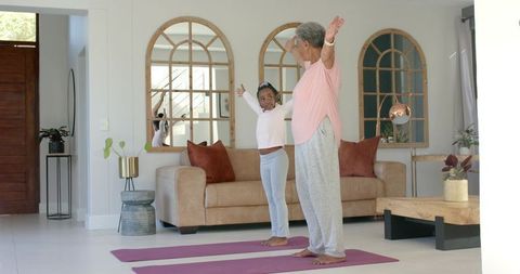 Black grandmother and granddaughter doing yoga together in sunlit living room