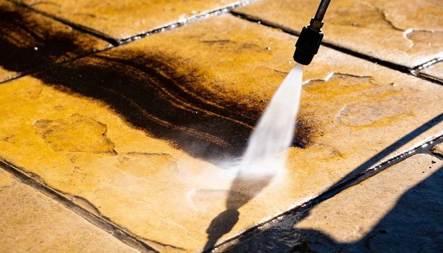 Power washing paving slabs removing dirt from concrete patio with high-pressure water jet