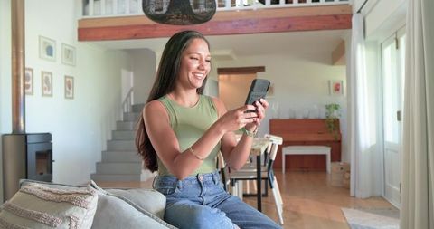 African american woman smiling and texting on smartphone in modern open-plan living room