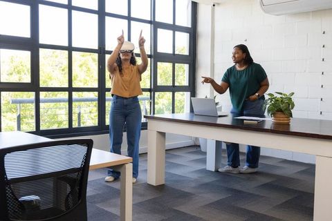 Diverse female coworkers collaborating with virtual reality headset in bright modern office