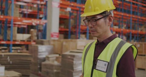 Korean Warehouse Inspector Wearing Yellow Helmet and Hi-Vis Vest Inspecting Racking