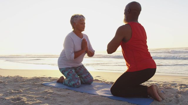 Senior couple engages in meditation and yoga practice on a sandy beach at sunrise. Effectively use this for promoting meditation practices, healthy lifestyles for seniors, beachside wellness retreats, or leisure wellness concepts.