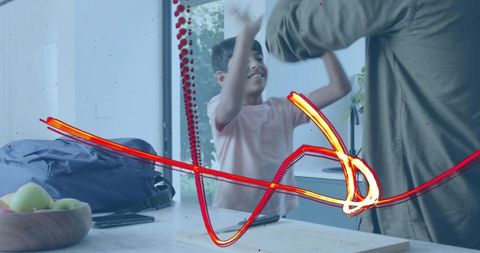 Playful boy high-fiving parent at kitchen counter with backpack and fruit bowl, morning