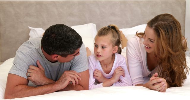 Parents and daughter lying on bed chatting at home in bedroom