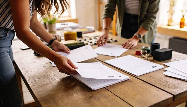 Sorting mail and organizing documents on rustic studio table, two women collaborating