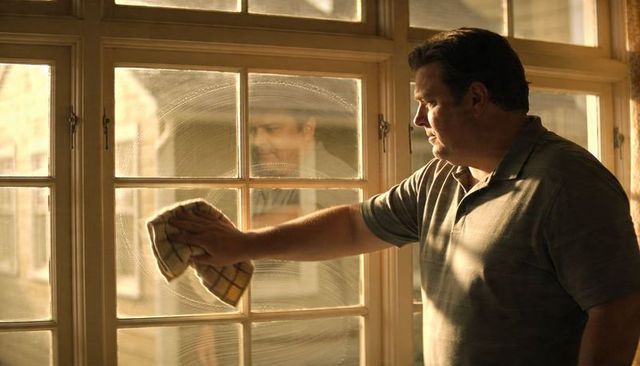 Middle-aged man wiping sunlit paned window with cloth cleaning indoor glass reflection