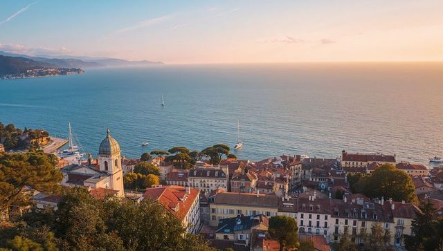 Sunlit mediterranean coastal town with red-tiled roofs, domed church and marina at sunset