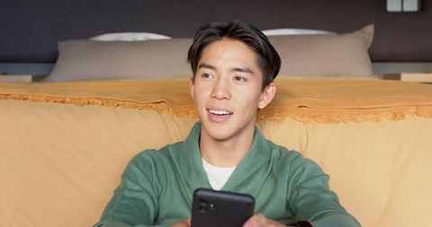 Young Asian Man Relaxing with Smartphone in Modern Bedroom