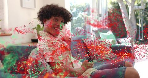 Smiling young man holding smartphone on sofa celebrating with vibrant confetti burst