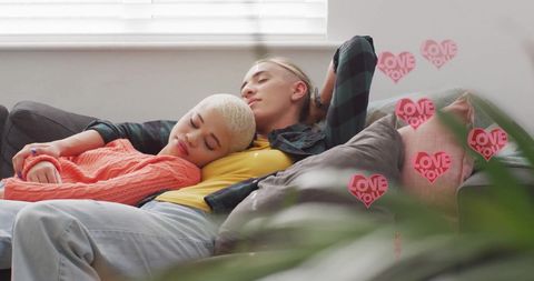this scene shows a diverse female couple comfortably resting at home, enveloped by digital overlays of heart-shaped 'love you' symbols, providing a warm and romantic atmosphere. the peaceful and intimate environment showcases affection and togetherness. ideal for use in depicting modern relationships, inclusivity, romance promotion, or cozy living space themes in lifestyle and digital communication context.