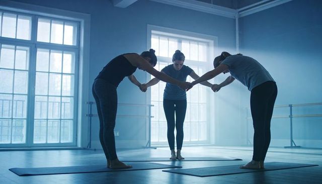 Three women holding hands while bowing in synchronized group yoga balance and connection