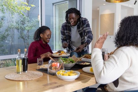 African american family sharing cozy dinner, man serving food with tongs in modern dining