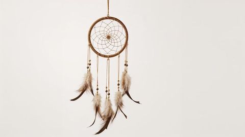 Hanging dreamcatcher with feathers against beige background