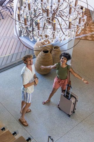 Couple admiring crystal chandelier in boutique lodge lobby arriving with suitcase