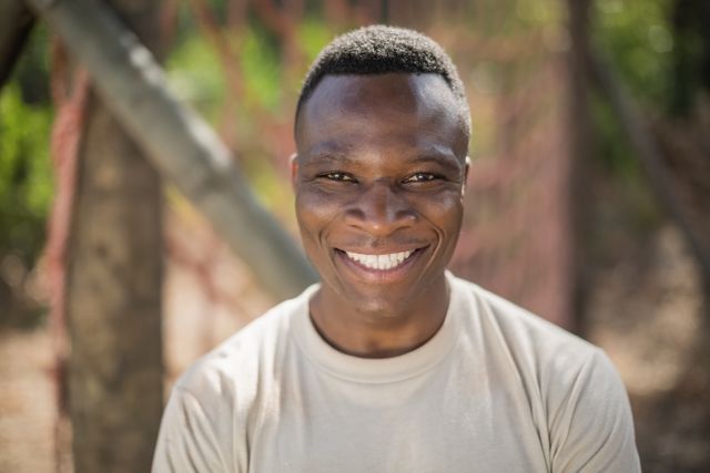 Smiling military soldier in boot camp, wearing uniform, looking confident and happy. Ideal for use in articles about military training, recruitment campaigns, motivational posters, and advertisements promoting strength and resilience.