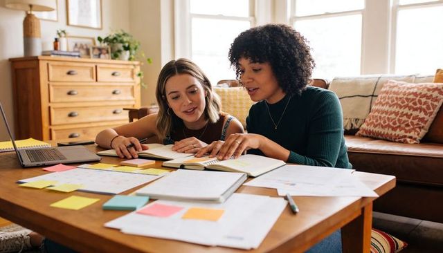 Two women studying together at coffee table planning with laptop and colorful sticky notes