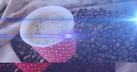 Showing red polka-dot cup with frothy coffee on roasted beans and burlap, blue lens flare