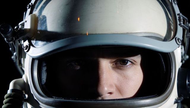 Close-up astronaut helmet portrait gazing forward dramatic low-light space explorer face
