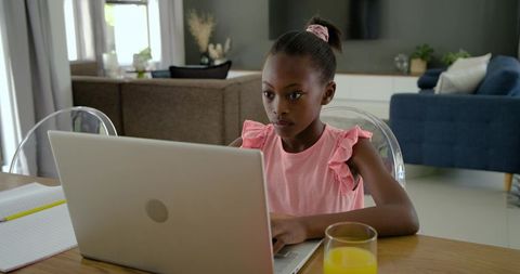 African girl studying online at home using laptop and taking notes with orange juice