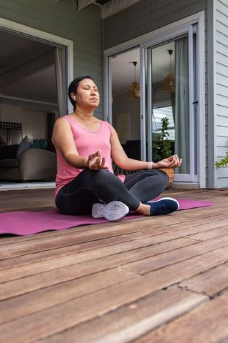 Porch meditation routine woman practicing mindfulness sitting cross-legged pink yoga mat