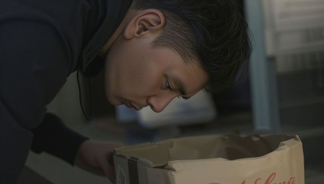 Leaning man inspecting dented cardboard box on metal shelf in warehouse storage inspection