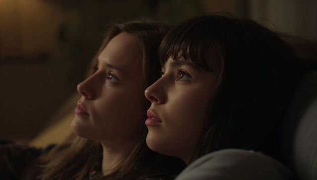 Two women reclining together on sofa gazing into distance warm cozy evening portrait vibe